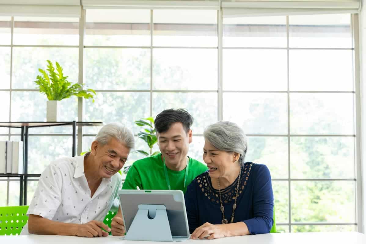 Three people smiling while looking at a tablet, discussing finances and learning how to set up a SMSF in a bright room.